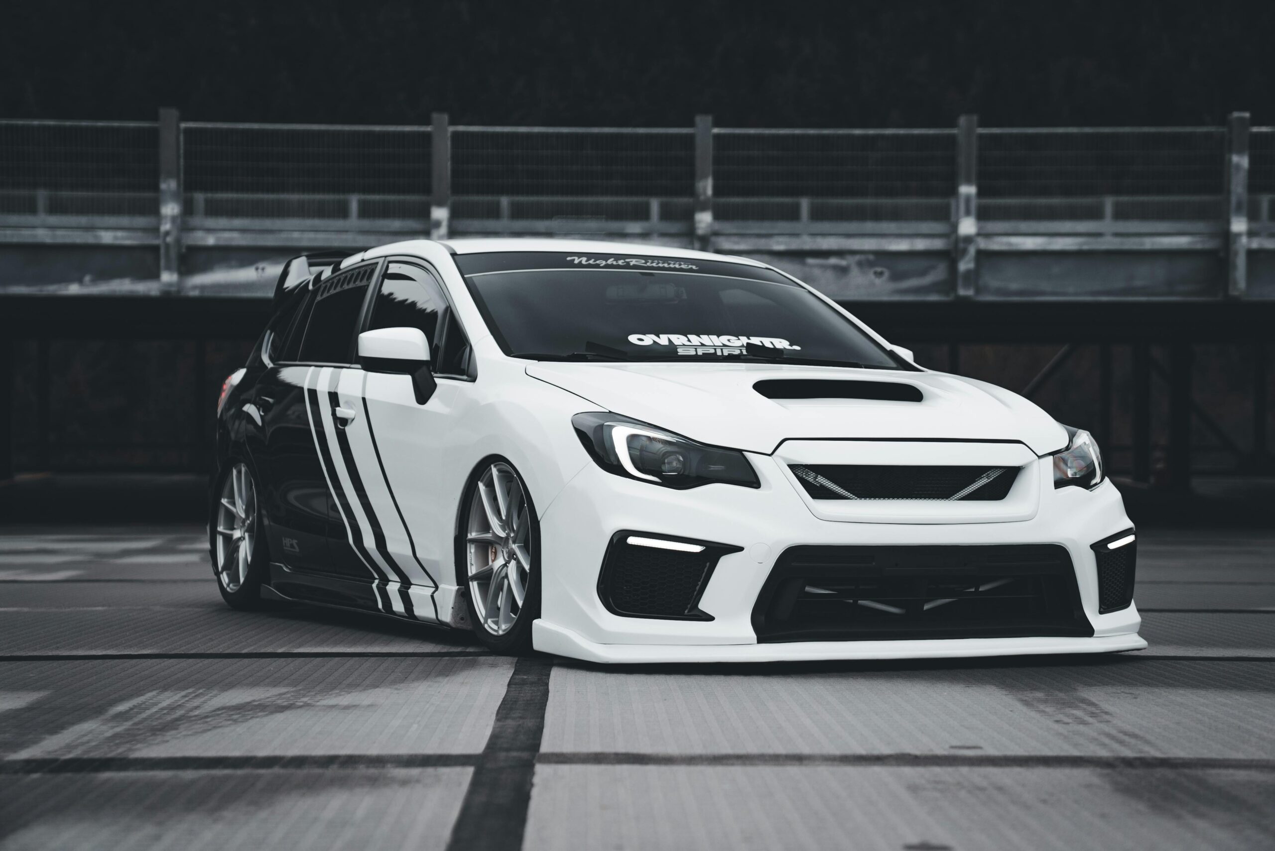 Stylish white sports car with black stripes parked outdoors, featuring custom modifications.